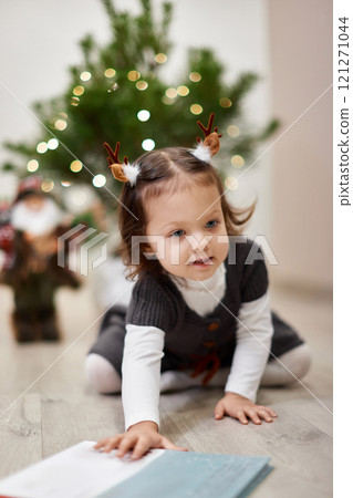 Cute little child girl reads a book near the Christmas tree at home 121271044