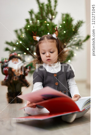 Cute little child girl reads Christmas stories and fairy tales near the Christmas tree at home 121271045