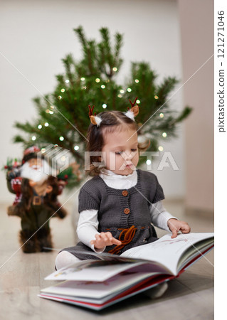 Cute little child girl reads Christmas stories and fairy tales near the Christmas tree at home 121271046