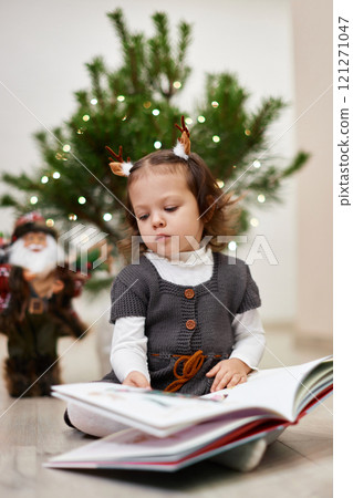 Cute little child girl reads a book near the Christmas tree at home 121271047