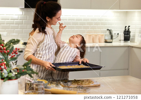 happy mother and little child daughter holding tray with gingerbread cookies in kitchen. Christmas time 121271058