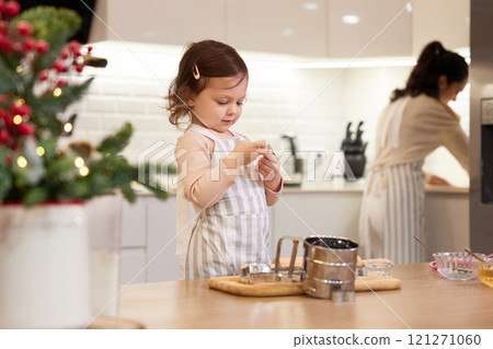 cute little child girl and her mother in aprons baking cookies in the kitchen, Christmas time 121271060
