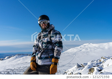 Satisfied man at the Sheregesh ski resort, against the backdrop of snowy slopes of mountain and blue sky at sunny day Satisfied man at the Sheregesh ski resort, against the backdrop of snowy slopes of mountain and blue sky at sunny day 121271350