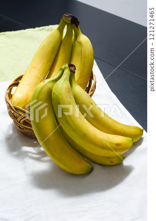 Ripe yellow bananas in a woven basket on a white cloth. 121271465