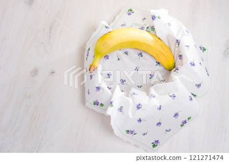 Ripe banana nestled in a floral napkin on a white wooden table. Ripe banana nestled in a floral napkin on a white wooden table. 121271474