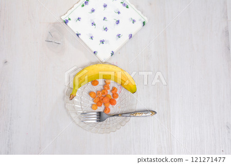 Banana, yellow raspberries, and a fork on a glass plate with a napkin. 121271477