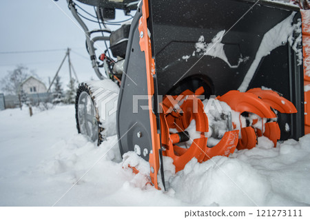 Close up photo of an orange petrol snow blower for private use. No recognizable parts or brands. In an ordinary snowy yard there is a gasoline snow blower . High quality photo 121273111