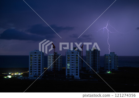 Lightning strikes over oceanfront construction at dusk in a vibrant coastal city skyline Lightning strikes over oceanfront construction at dusk in a vibrant coastal city skyline 121274356