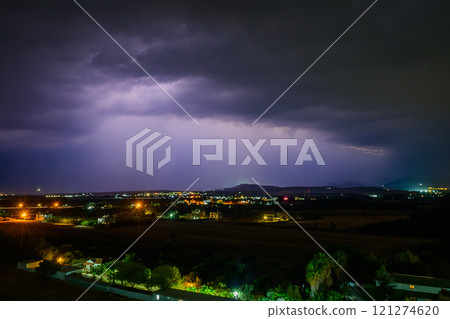 A thunderous night sky illuminates the landscape with flashes of lightning over a quiet town. A thunderous night sky illuminates the landscape with flashes of lightning over a quiet town. 121274620