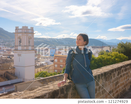 Young woman exploring historic castle in Denia, Alicante province, Spain, scenic views of town below, set against cooler season backdrop. blend of history and tranquility in timeless setting. Young woman exploring historic castle in Denia, Alicante province, Spain, scenic views of town below, set against cooler season backdrop. blend of history and tranquility in timeless setting. 121274929