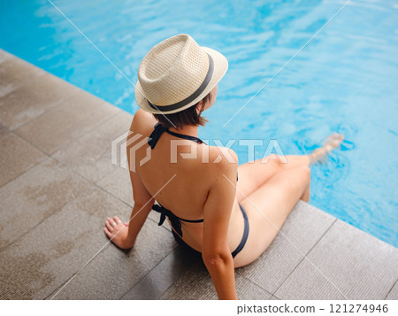 Young asian woman relaxing by pool at Kuala Lumpur hotel with view of surrounding skyscrapers, enjoying leisure time in vibrant urban setting. 121274946