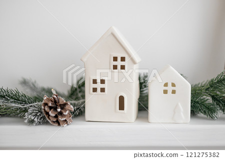 Atmospheric Christmas scene, miniature holiday houses. Scandinavian white houses on a desk in the home interior of the living room. Cozy concept of festive decoration of the house. Atmospheric Christmas scene, miniature holiday houses. Scandinavian white houses on a desk in the home interior of the living room. Cozy concept of festive decoration of the house. 121275382