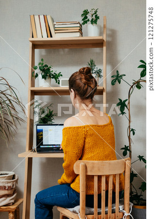 view from back, woman is sitting at desk in home office, working online. 121275748