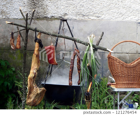 Cooking food in a boiling pot suspended from metal tripod. Kitchen in courtyard by wall on the fire 121276454