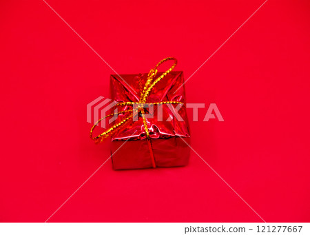 A red gift box with a gold ribbon on a striking red background 121277667