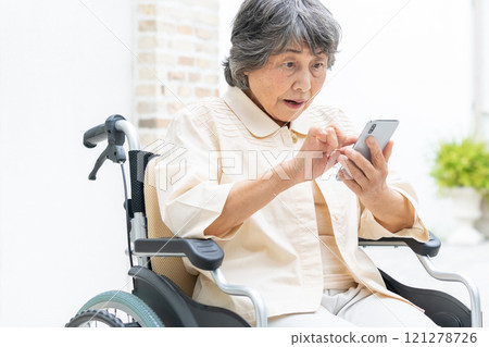 Senior woman in a wheelchair operating a smartphone Senior woman in a wheelchair operating a smartphone 121278726
