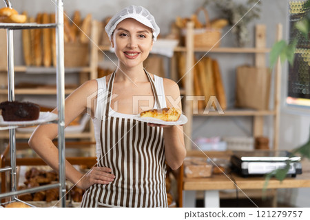 Young saleswoman holding piece of pastry in paper plate Young saleswoman holding piece of pastry in paper plate 121279757