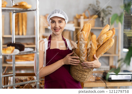 Young saleswoman holding baguettes in wicker basket Young saleswoman holding baguettes in wicker basket 121279758