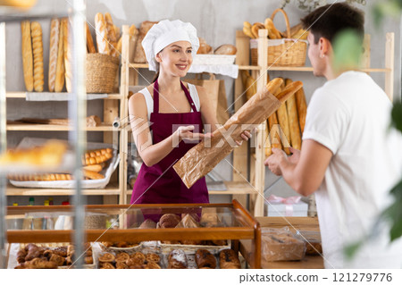 Smiling saleswoman offering fresh baguettes to customer in bakery Smiling saleswoman offering fresh baguettes to customer in bakery 121279776