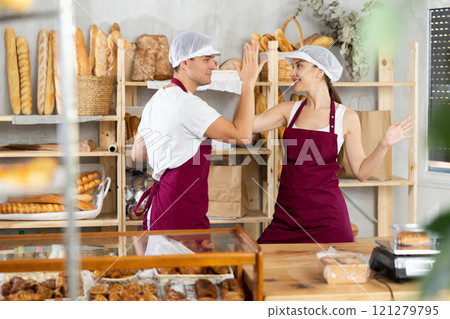 Girl and guy sellers in bakery are having fun and taking break from work, dancing and jumping. Girl and guy sellers in bakery are having fun and taking break from work, dancing and jumping. 121279795