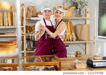Girl and guy sellers in bakery are having fun and taking break from work, dancing and jumping. Girl and guy sellers in bakery are having fun and taking break from work, dancing and jumping. 121279796