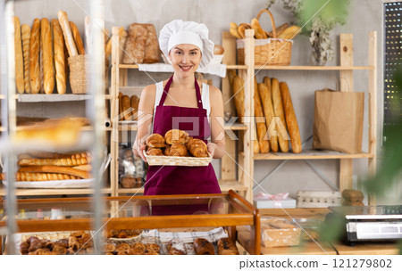 Young saleswoman displays croissants in square wicker basket 121279802