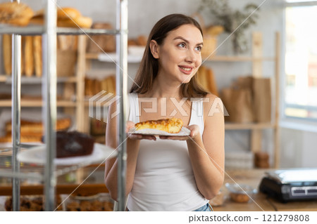 Positive young girl holding pastry on paper plate in bakery 121279808