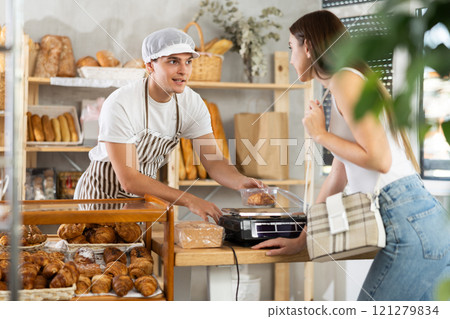 Young bakery worker weighing pastries for female customer Young bakery worker weighing pastries for female customer 121279834