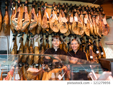 Butcher shop owner and assistant sell Spanish ham 121279956