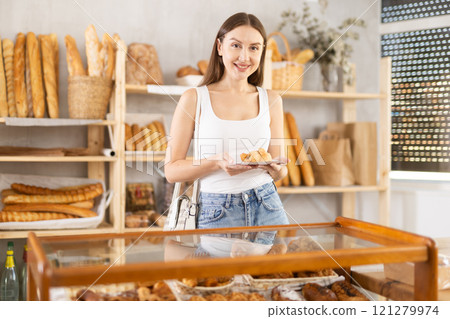 Satisfied female customer selects fresh croissants at display window of bakery 121279974