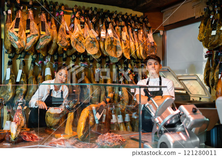 Young man and woman selling spanish jamon at counter Young man and woman selling spanish jamon at counter 121280011