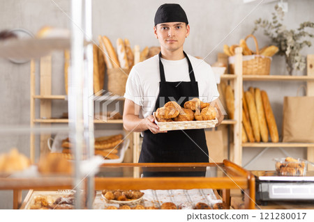Smiling young baker offering freshly baked croissants 121280017