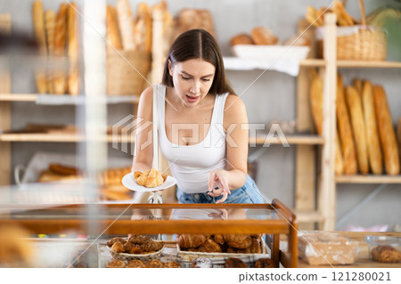 Young woman buyer chooses pastries in bakery 121280021