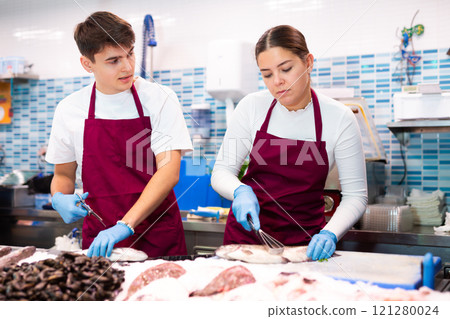 Proficient sellers processing seabass on table board in fish store 121280024
