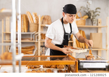 Young male seller puts disposable plastic box with buns on scales 121280025