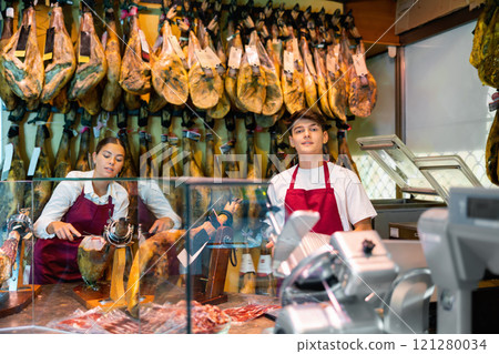 Young couple work together in butcher shop - they cut traditional Spanish jamon 121280034