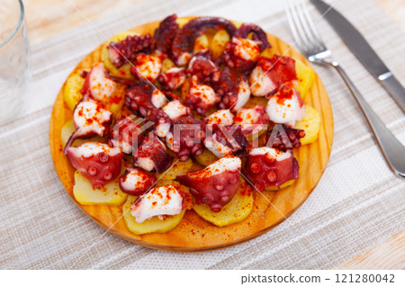 Chopped cooked octopus tentacles with smoked paprika and potato on wooden board 121280042