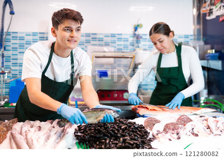 Seller in apron shows hands fish trout on counter in supermarket 121280082