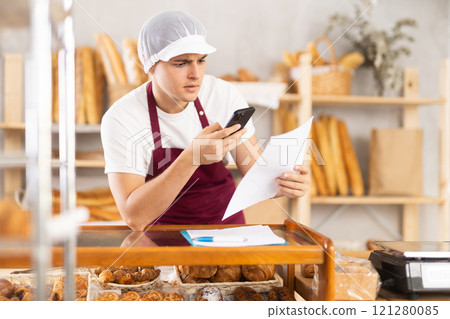 Focused young bakery manager organizing orders with smartphone Focused young bakery manager organizing orders with smartphone 121280085