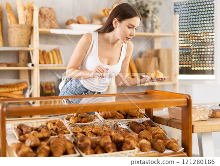 Satisfied female customer selects fresh croissants at display window of bakery 121280186