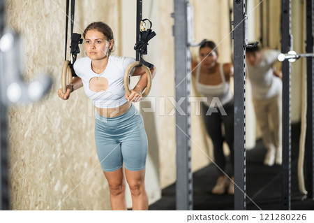 Girl trains on gymnastic rings in modern crossfit gym 121280226