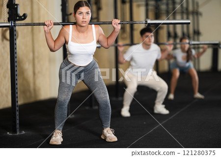 Girl in activewear exercising with barbell during group workout in gym center 121280375