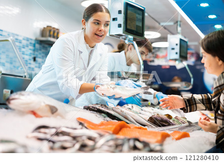 Positive saleswoman demonstrating seabass in fish store Positive saleswoman demonstrating seabass in fish store 121280410