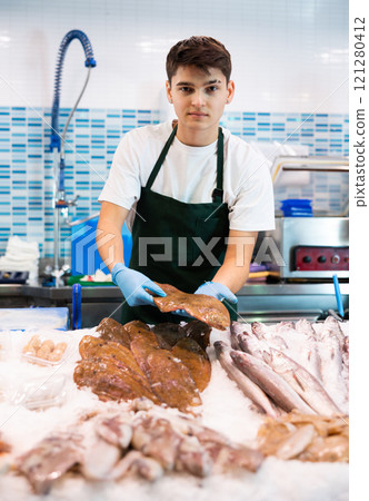 Portrait of man offering fresh fish flounder at seafood shop 121280412