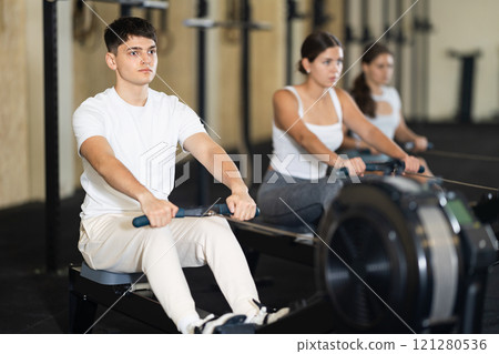 Athletic guy in sportswear training on rowing machine in gym 121280536