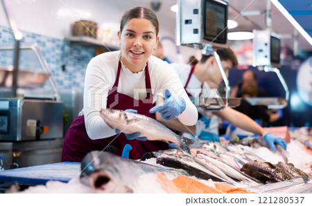Woman seller of fish advises buyer to buy hake fresh fish 121280537