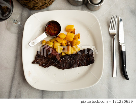 Slice of beef meat served on plate with baked potatoes on side and sauce Slice of beef meat served on plate with baked potatoes on side and sauce 121280639