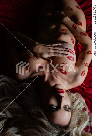 Intimate topless woman adorned with body art rests on a red surface Intimate topless woman adorned with body art rests on a red surface 121281703