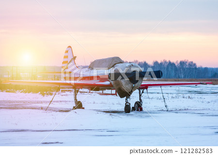Small sports airplane on the apron of a snowy airfield in cold winter sunset 121282583