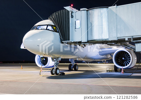 A white passenger aircraft stands at the boarding bridge connected to an external power supply on an airport night apron 121282586